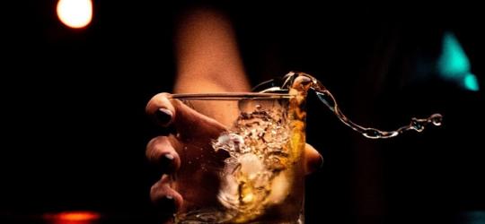 Kobieca ręka z impetem stawia szklankę z alkoholem na stół, płyn się rozlewa.